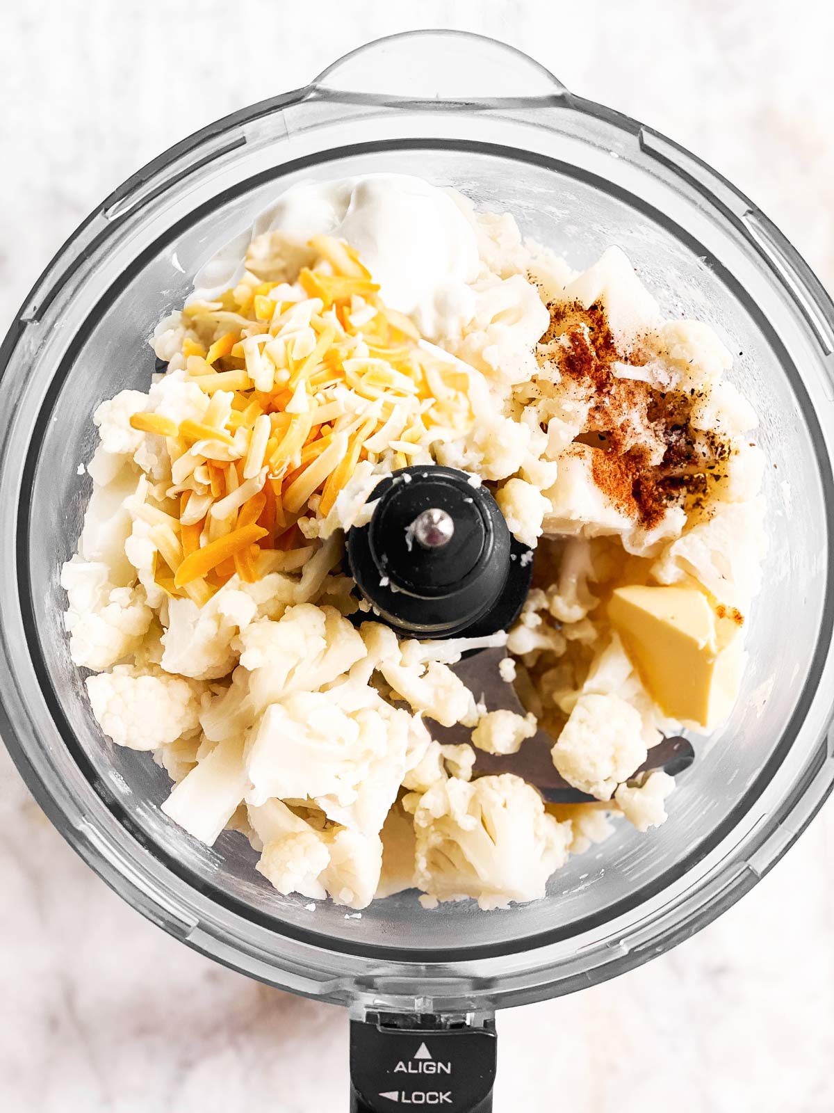 food processor with cooked cauliflower, cheese, sour cream and seasoning