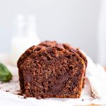 sliced chocolate zucchini bread on a wooden board with a bottle of milk