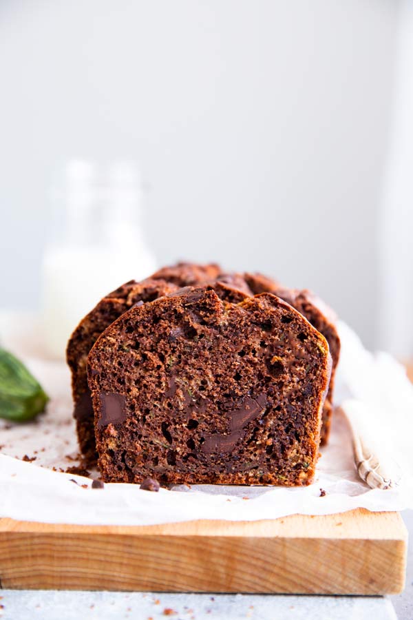 sliced chocolate zucchini bread on a wooden board with a bottle of milk