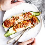 female hands holding plate with two keto zucchini boats