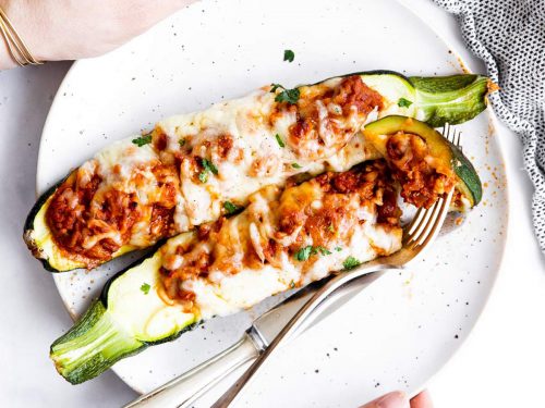 female hands holding plate with two keto zucchini boats