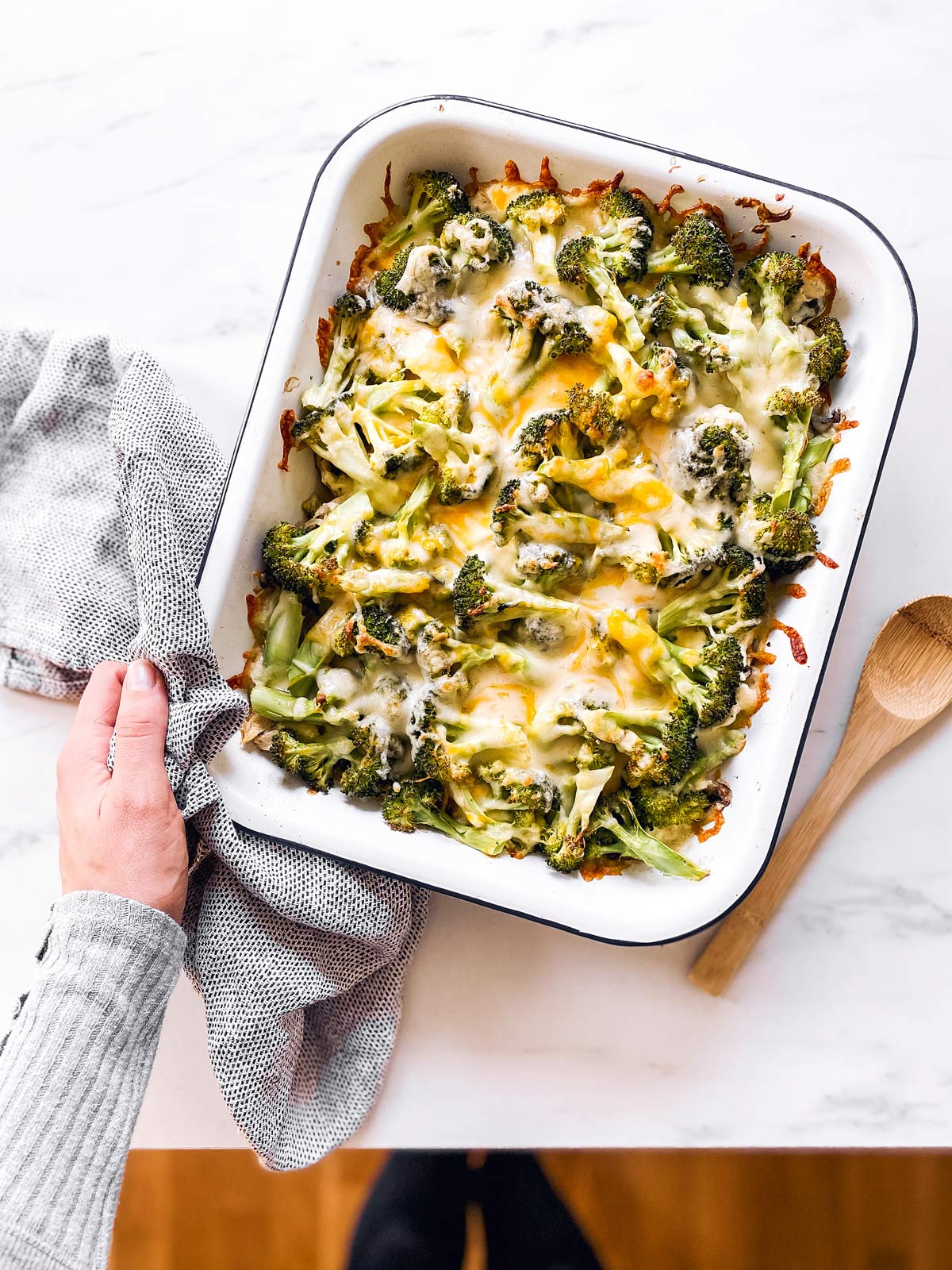 female hand holding casserole dish with baked chicken and broccoli