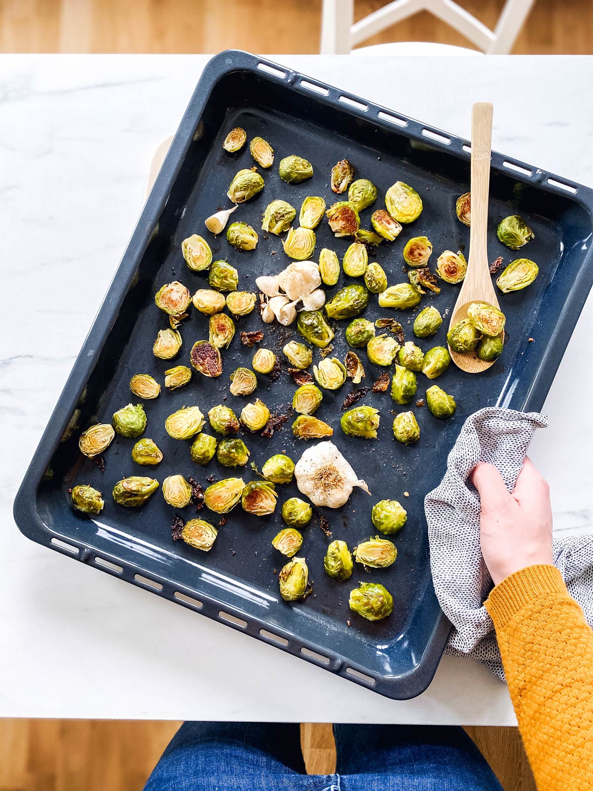 female hand holding a sheet pan with roasted Brussels sprouts