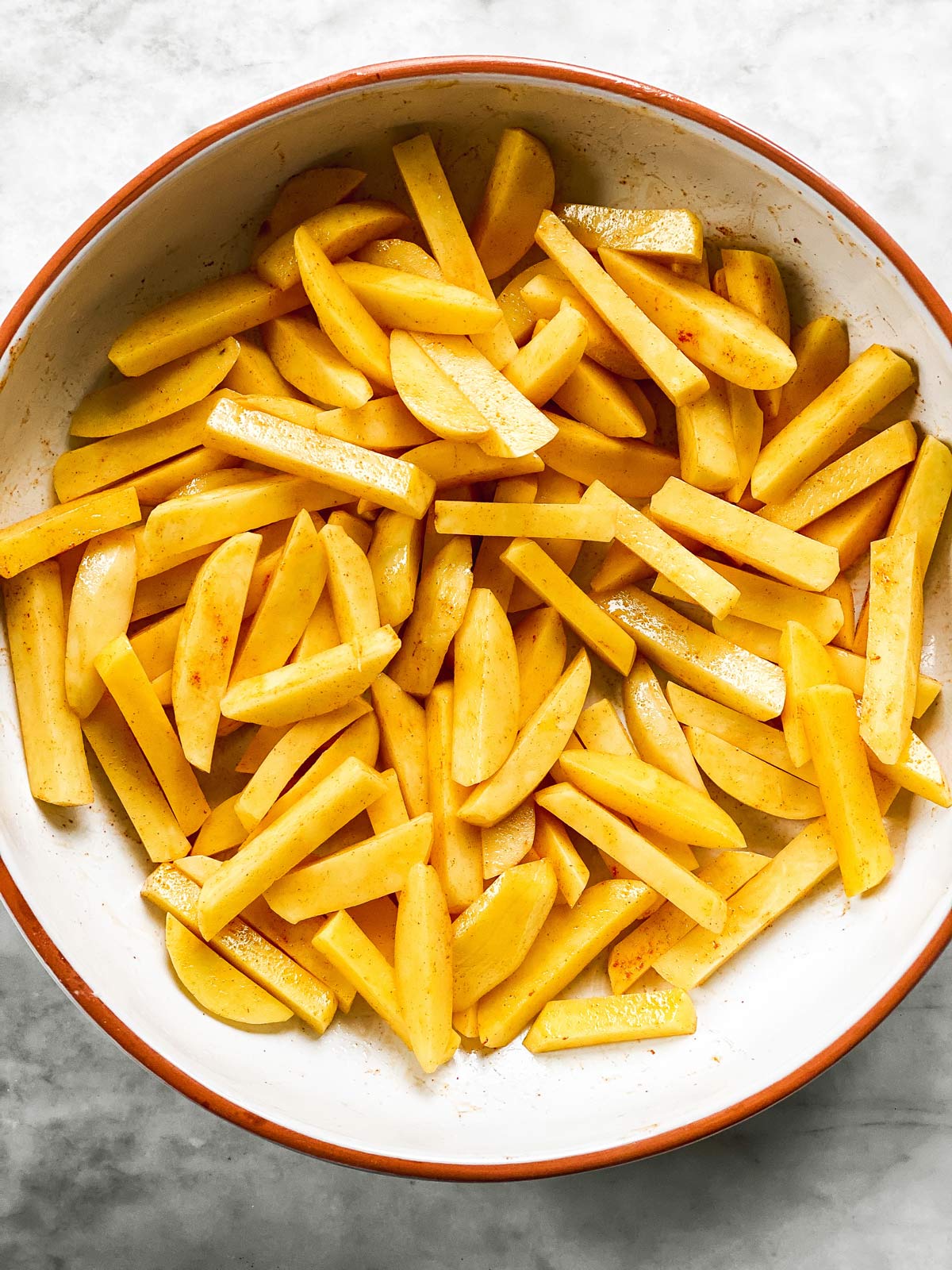 seasoned potatoes sliced into fries in large white bowl