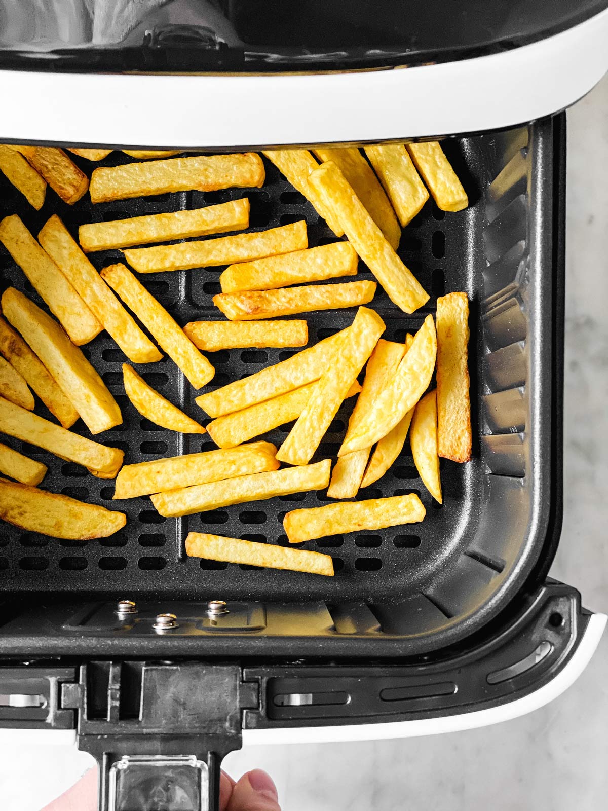 female hand shaking air fryer basket with fries