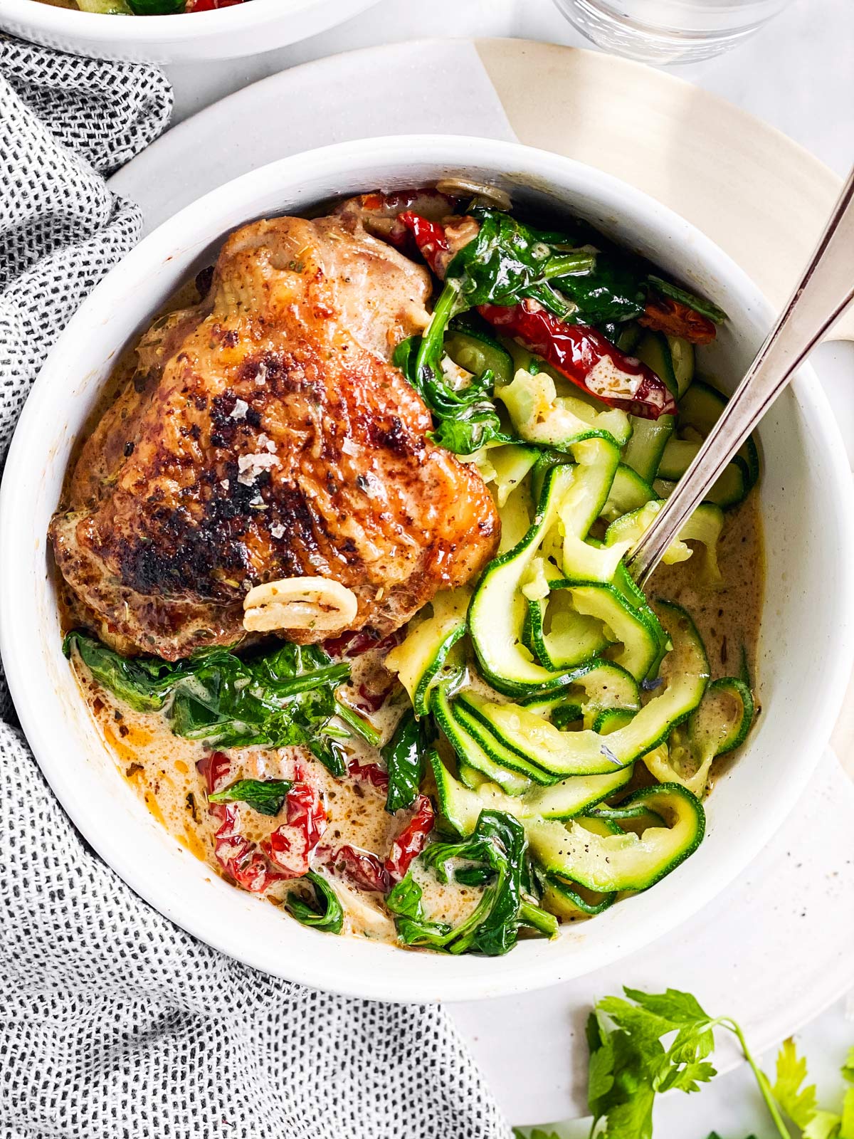 close up photo of white bowl with zucchini ribbons and tuscan chicken thighs