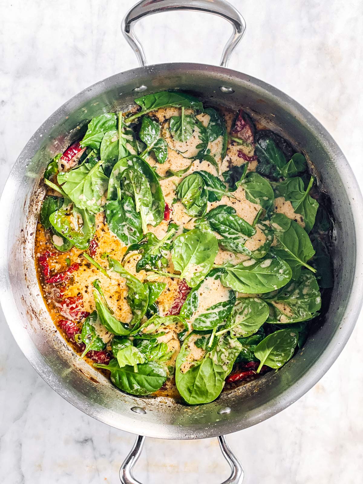 skillet with cream sauce and raw spinach