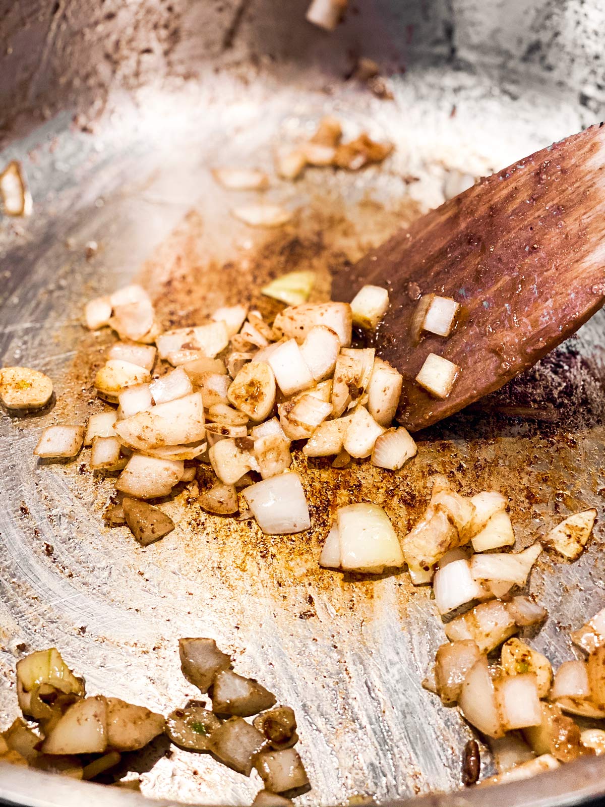 close up photo of cooked onion and garlic in skillet with wooden spoon