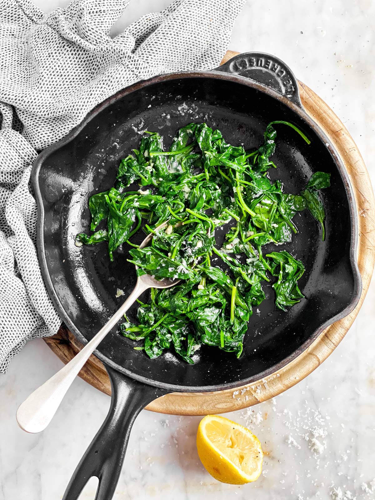 skillet with sautéed spinach and spoon on wooden board