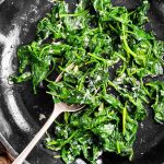 close up photo of sautéed spinach in a black skillet with a spoon