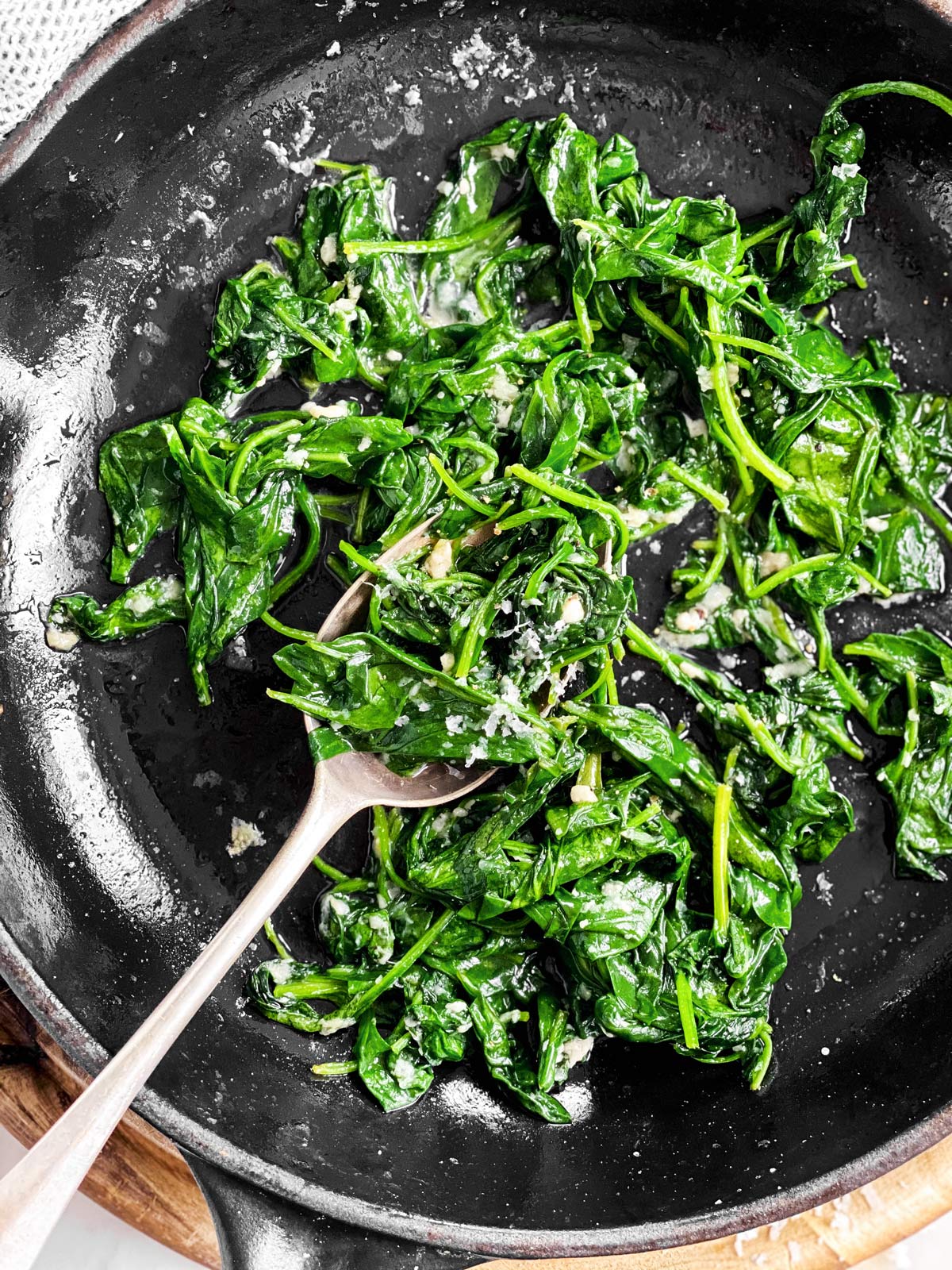 close up photo of sautéed spinach in a black skillet with a spoon